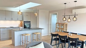 A modern kitchen with a central island, bar stools, and a dining area with a wooden table and chairs. - 4 Person Holiday Home in Allinge (Allinge)