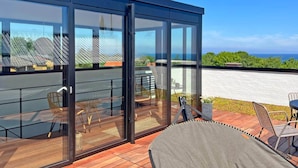 A modern outdoor deck with glass walls, a wooden floor, and outdoor furniture. - 4 Person Holiday Home in Allinge (Allinge)