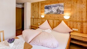 A bedroom with a wooden headboard, a bed with pink bedding, a painting above the bed, and a small table with a vase of flowers. - Comfortable Apartment in Langenfeld With ski Storage (Laengenfeld)