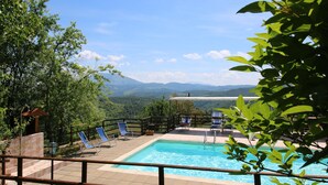 Ein Poolbereich mit Bergblick, umgeben von viel Grün und einem Holzzaun.