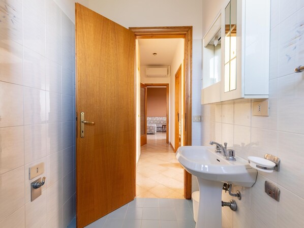 Un baño moderno con puerta de madera, lavamanos con espejo y suelo de baldosas.