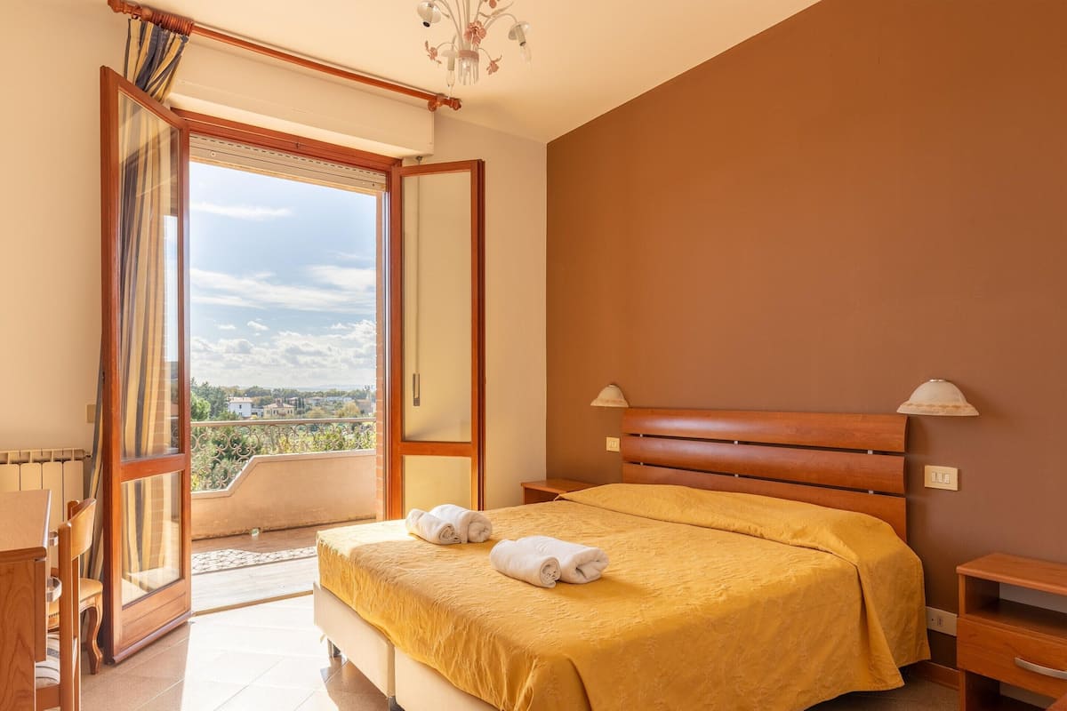 Un dormitorio con una cama grande, cabecera de madera, mesita de noche y vistas de la ciudad a través de una puerta abierta.