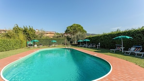 Une piscine bordée de briques, entourée de parasols verts et de chaises longues.