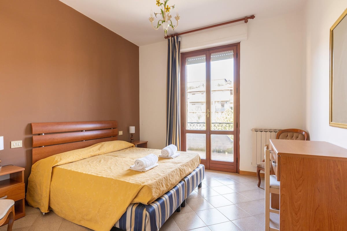 Habitación de hotel con cama, escritorio, silla, cómoda y ventana con vistas a edificios.