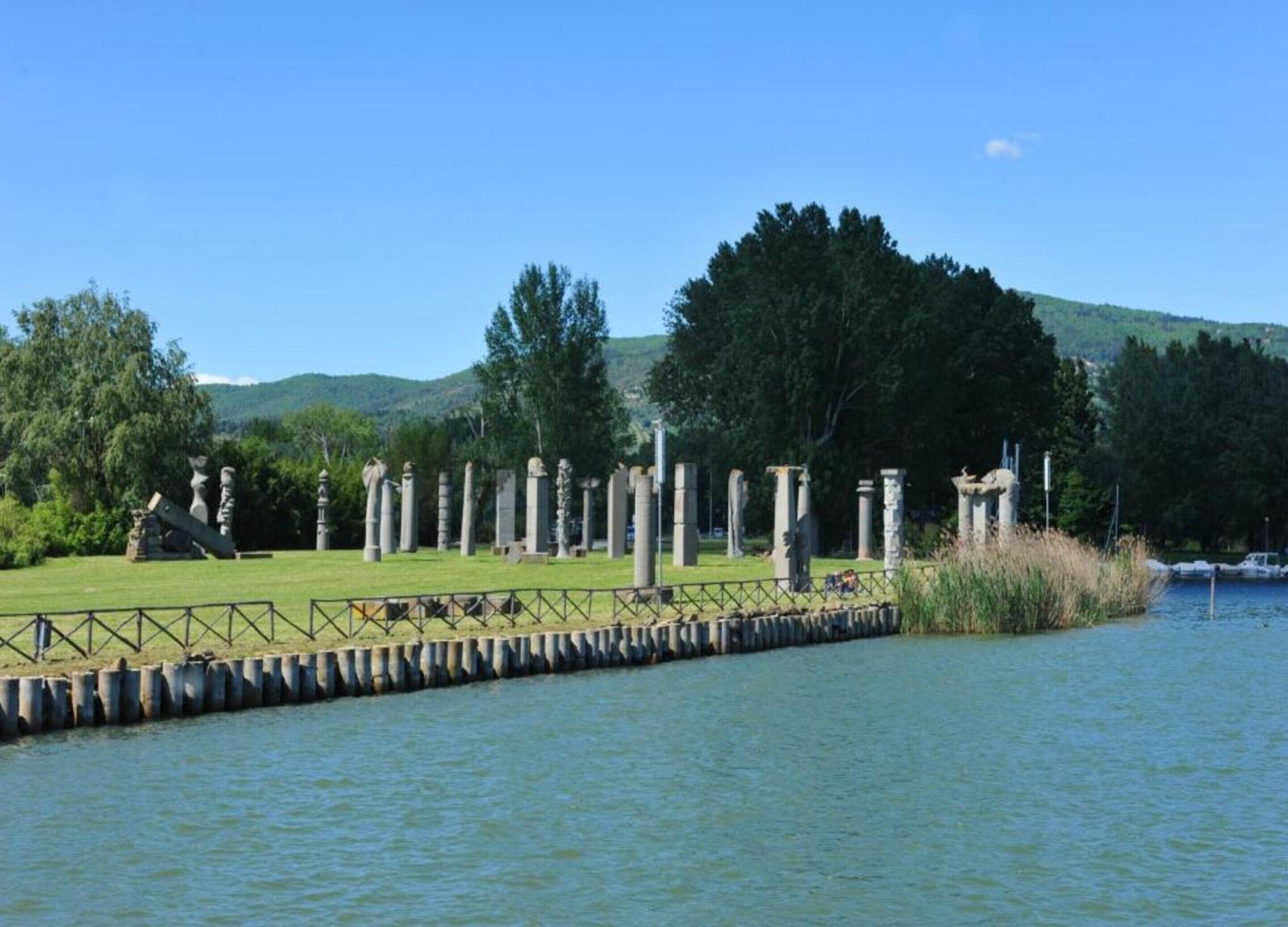 A serene lakeside setting with ancient stone columns and a grassy area.