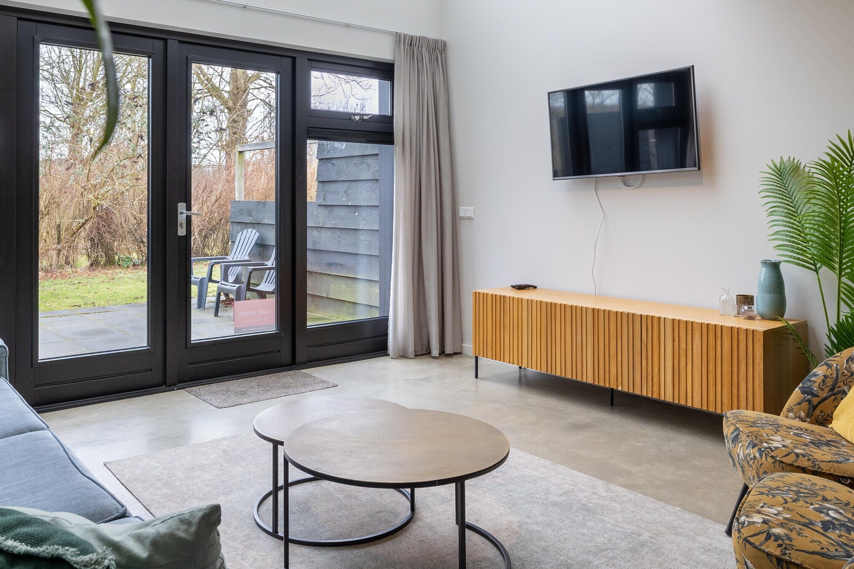 Ein modernes Wohnzimmer mit einer Schiebetür zum Patio, einem wandmontierten Flachbildfernseher, einem Holzkonsolentisch und einem gemusterten Sofa.