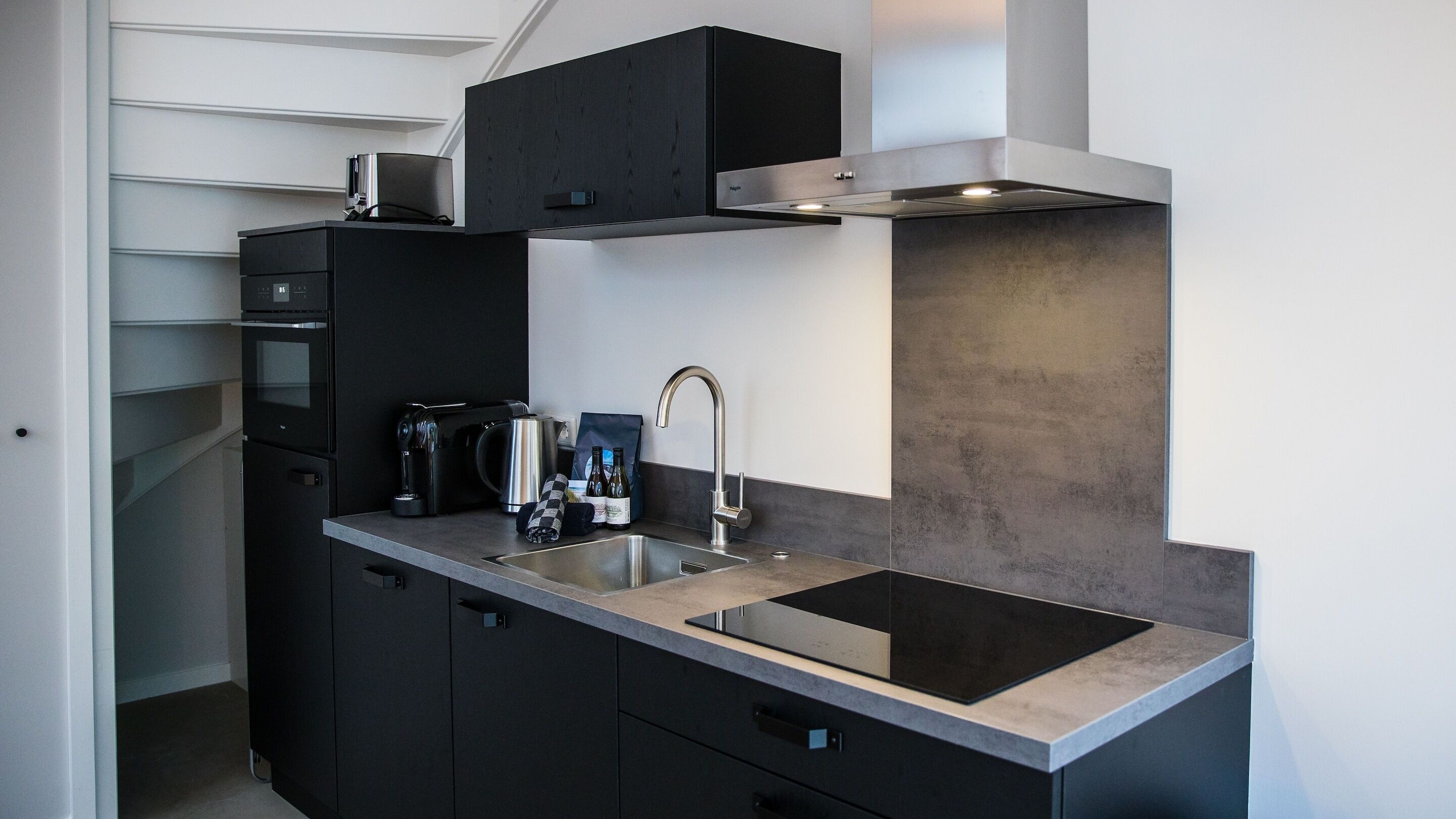 A modern kitchen with black cabinets, a stainless steel sink, and a built-in range hood.