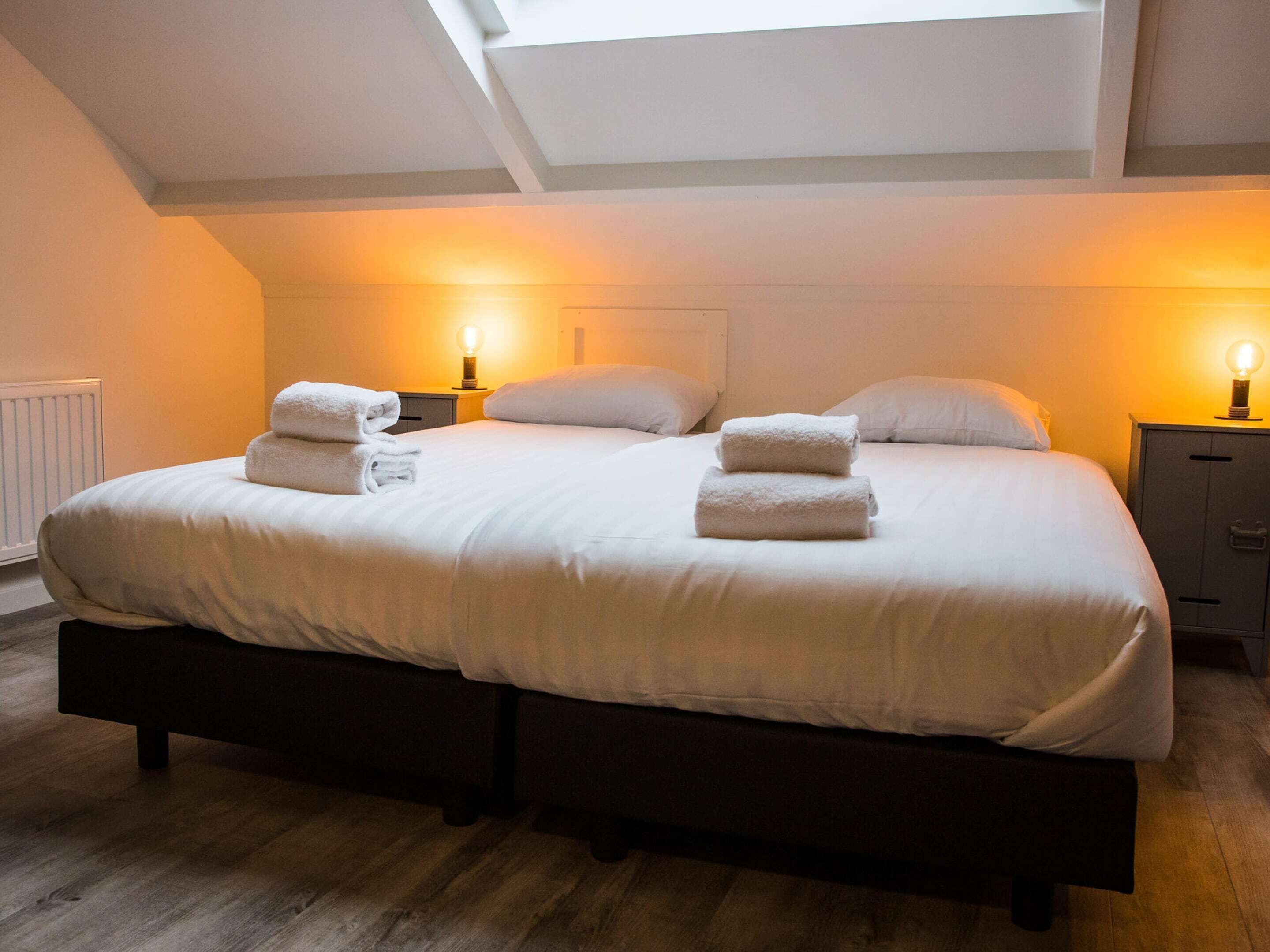 A double bed with two sets of towels, a bedside table with a lamp, and a radiator.