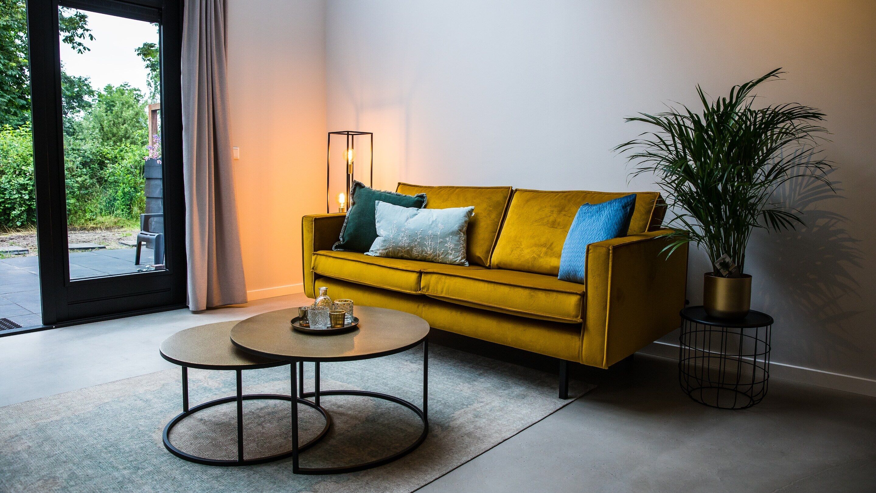 Un salon moderne avec un canapé jaune moutarde, une table basse ronde et une grande plante en pot.