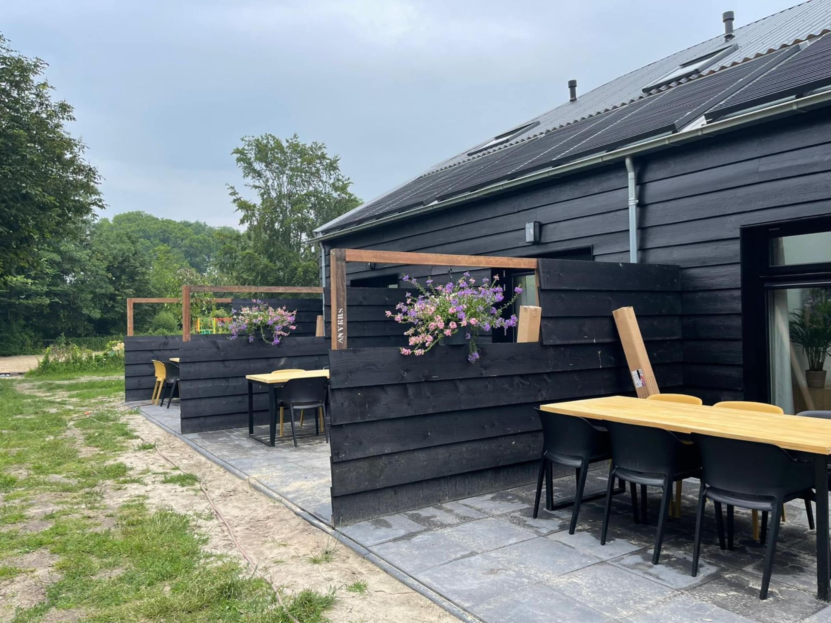 A wooden building with a patio area, outdoor seating, and hanging flowers.
