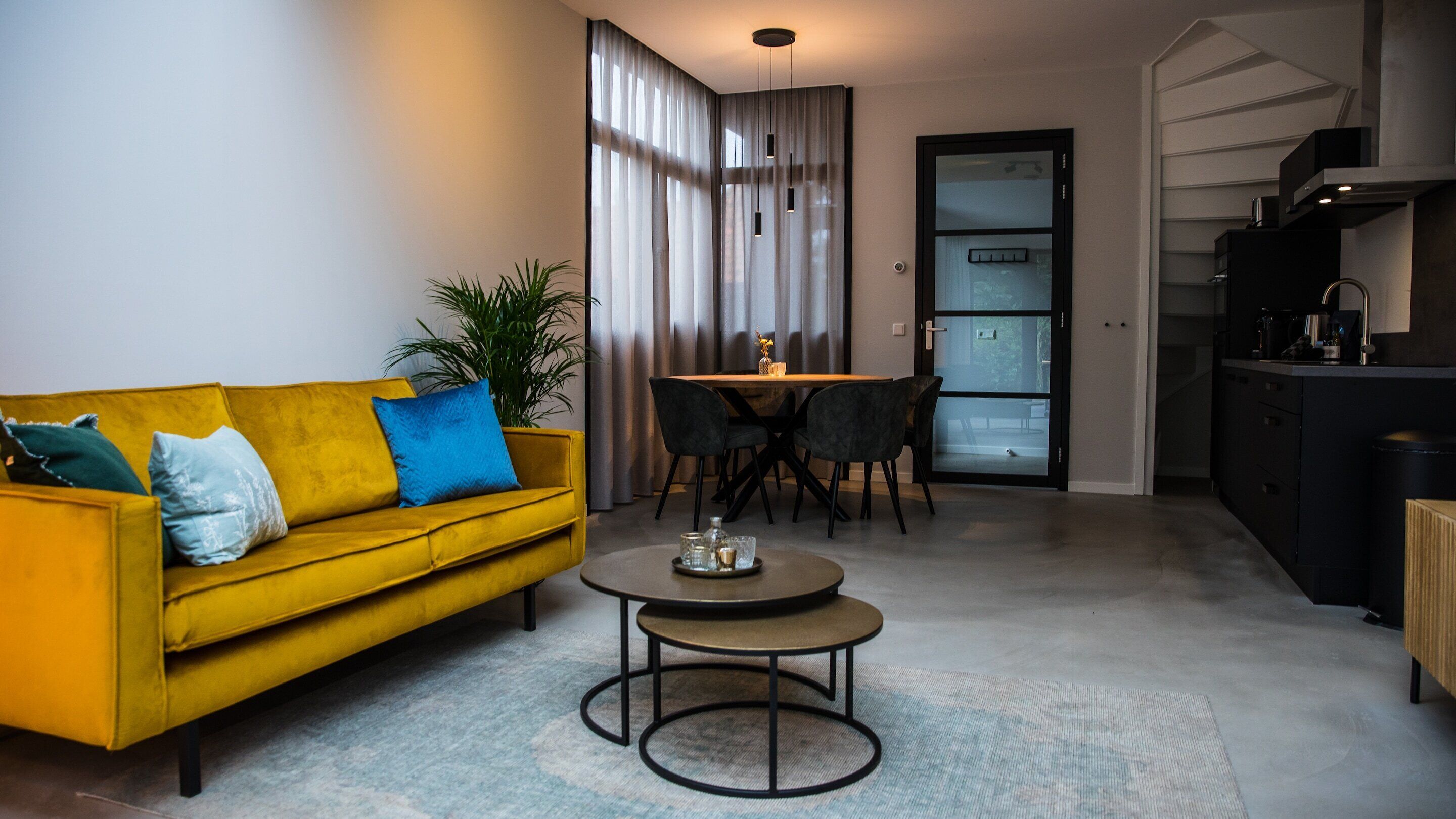 Un salon moderne avec un canapé jaune, une table basse ronde et un coin repas doté d’une porte en verre.