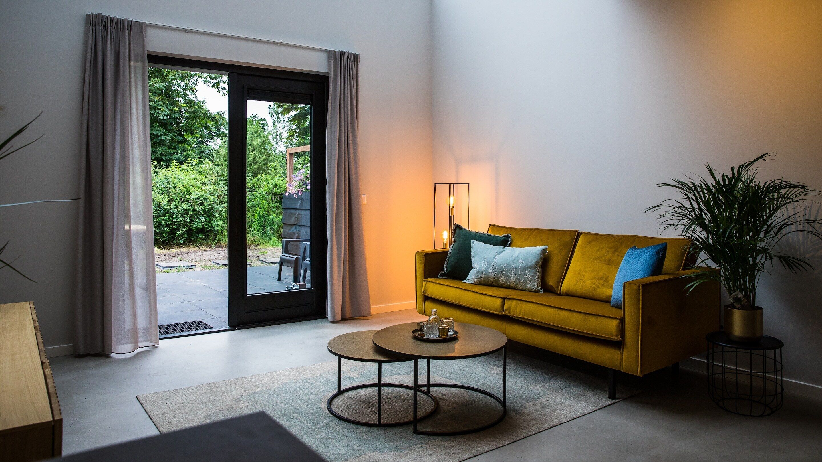 A modern living room with a yellow sofa, a coffee table, and a large window with curtains.