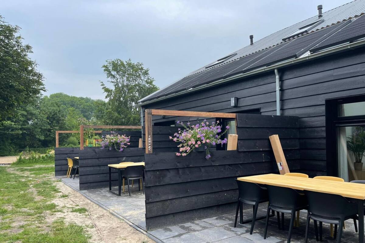 A wooden building with a patio area, outdoor seating, and hanging flowers.