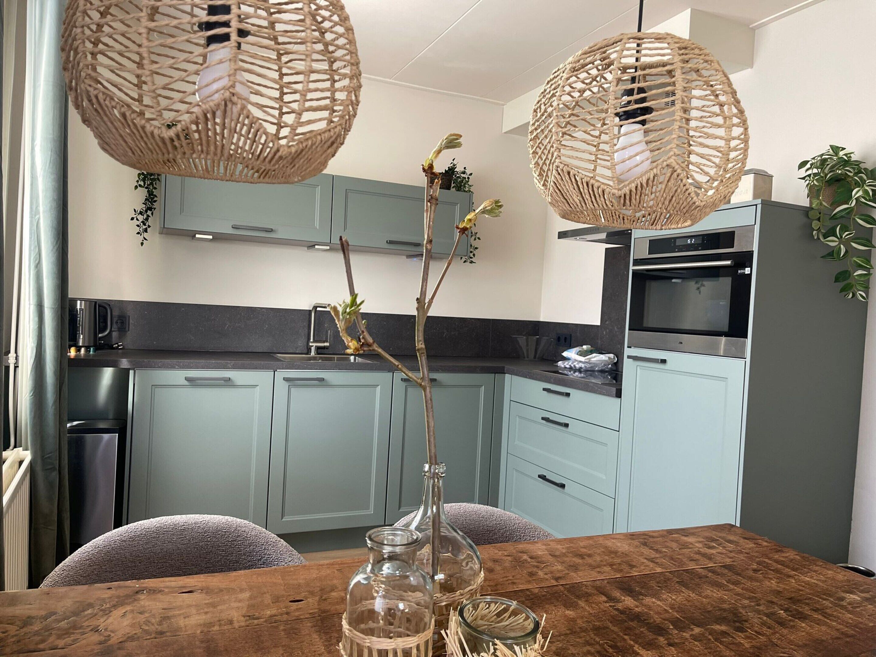 A modern kitchen with light blue cabinets, a wooden dining table, and two woven pendant lights.