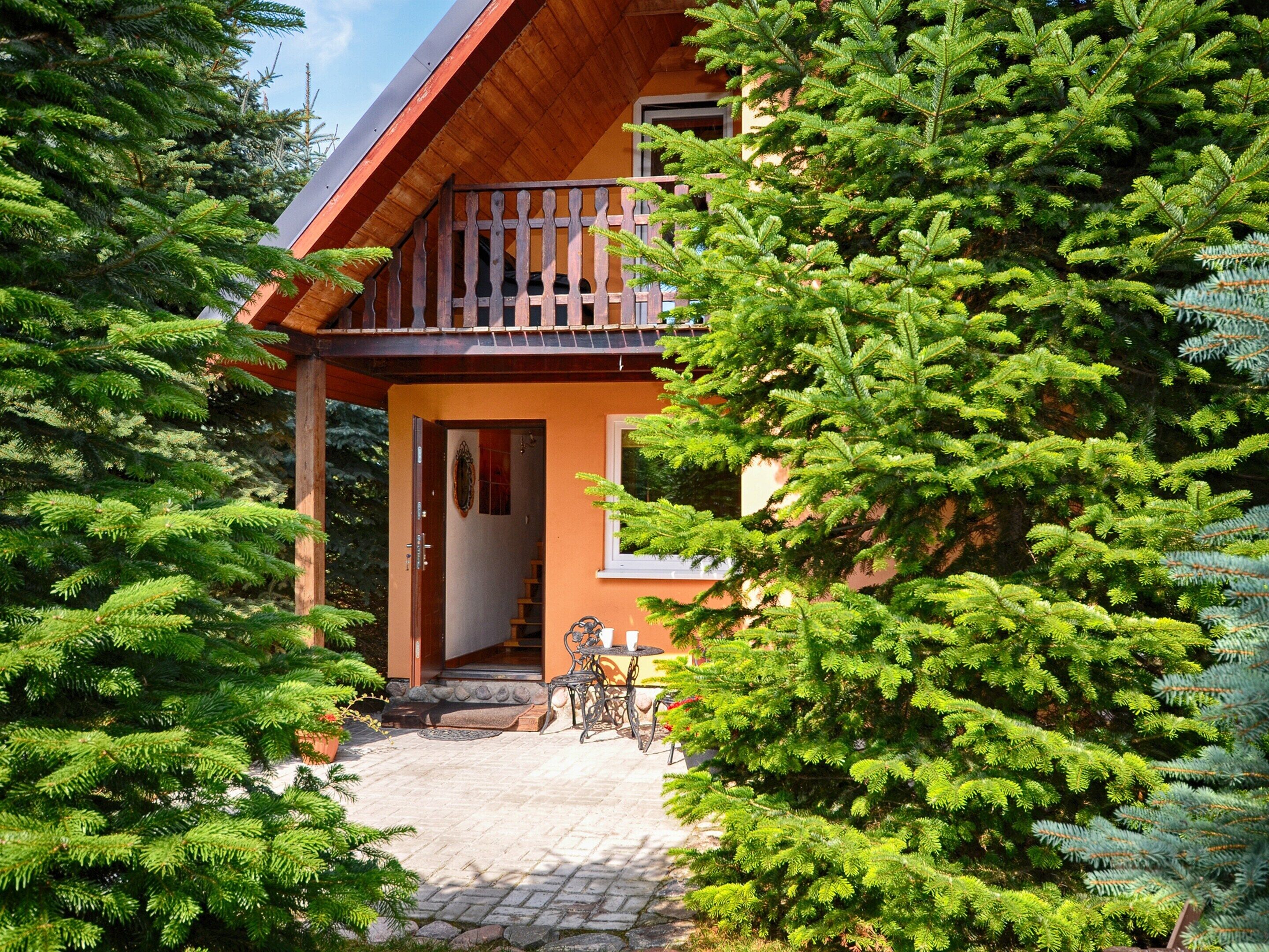 A wooden house with a balcony, surrounded by evergreen trees.
