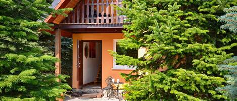A wooden house with a balcony, surrounded by evergreen trees.