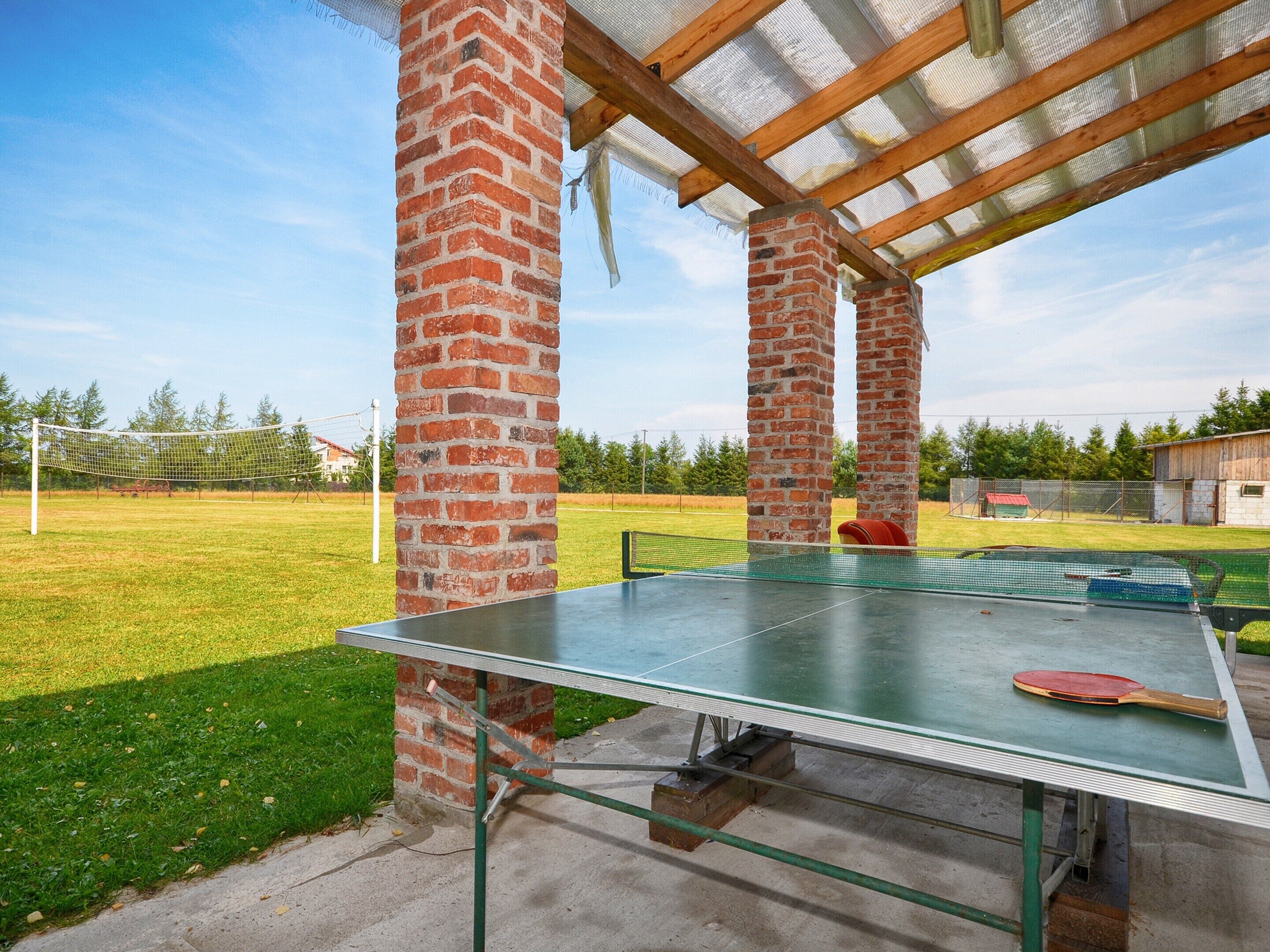 An outdoor ping pong table under a covered area with brick pillars.