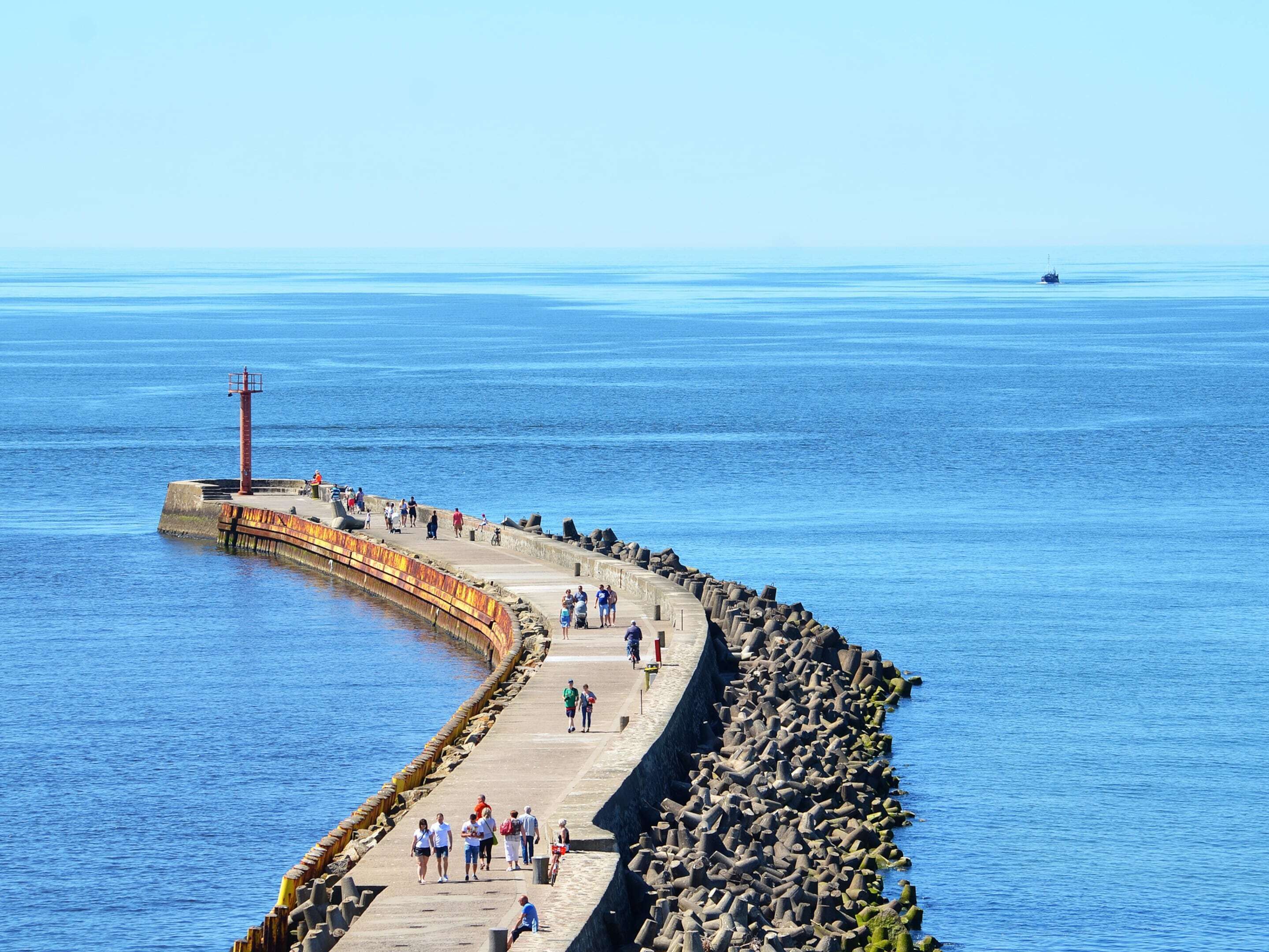 Ein Küstenweg mit einer gewundenen Steinmauer, einem roten Leuchtturm und freiem Blick auf das Meer.