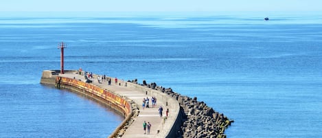 Ein Küstenweg mit einer gewundenen Steinmauer, einem roten Leuchtturm und freiem Blick auf das Meer.