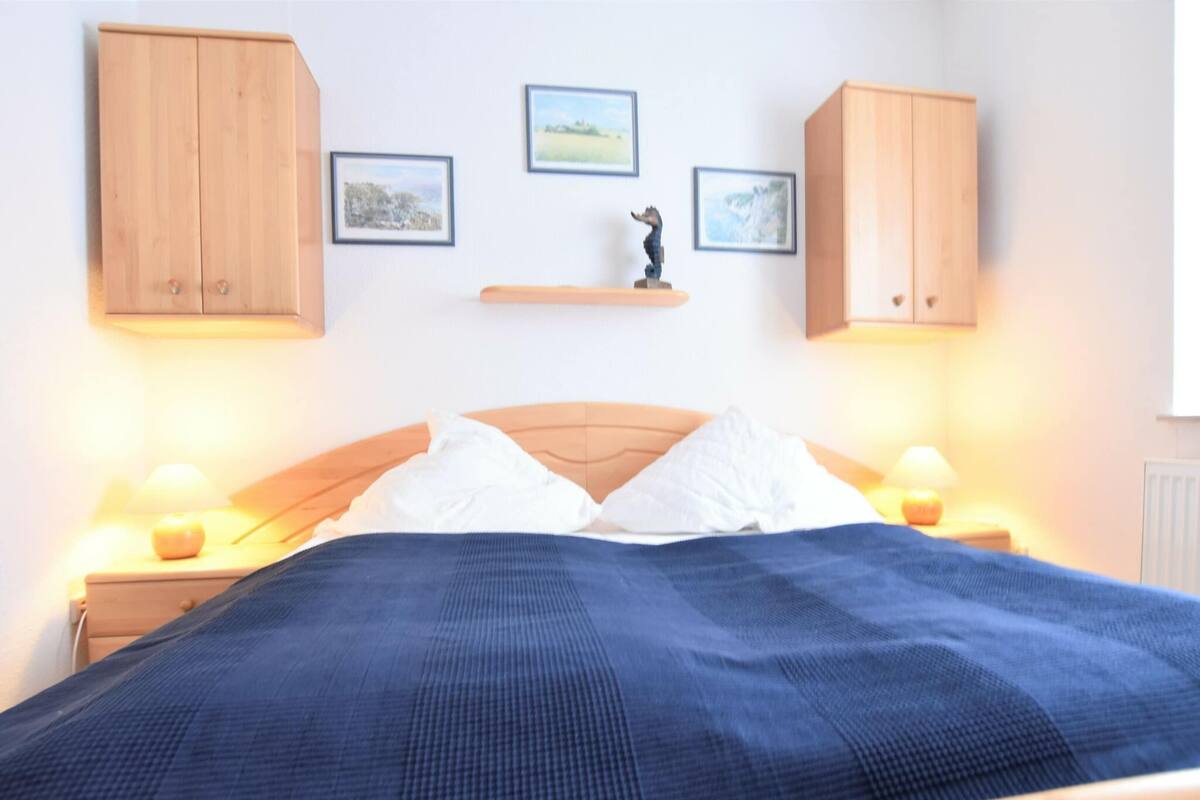 A bedroom with a wooden bed, two nightstands with lamps, a blue bedspread, and three framed pictures on the wall.