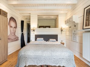 A bedroom with a large bed, wooden floors, a mirror, and wall-mounted lights. - Holiday Home in West Flanders With Garden and Bubble Bath (Pittem)