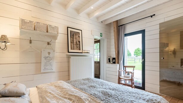 A bedroom with a bed, a chair, a radiator, and a door leading to a balcony. - Holiday Home in West Flanders With Garden and Bubble Bath (Pittem)