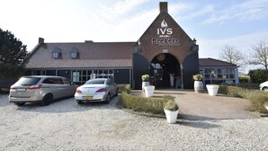 A building with a sign reading "IVS Bar & Grill" and a brick facade. There are two cars parked in front. - Studio Hazenborgh in Callantsoog Near the sea (Callantsoog)