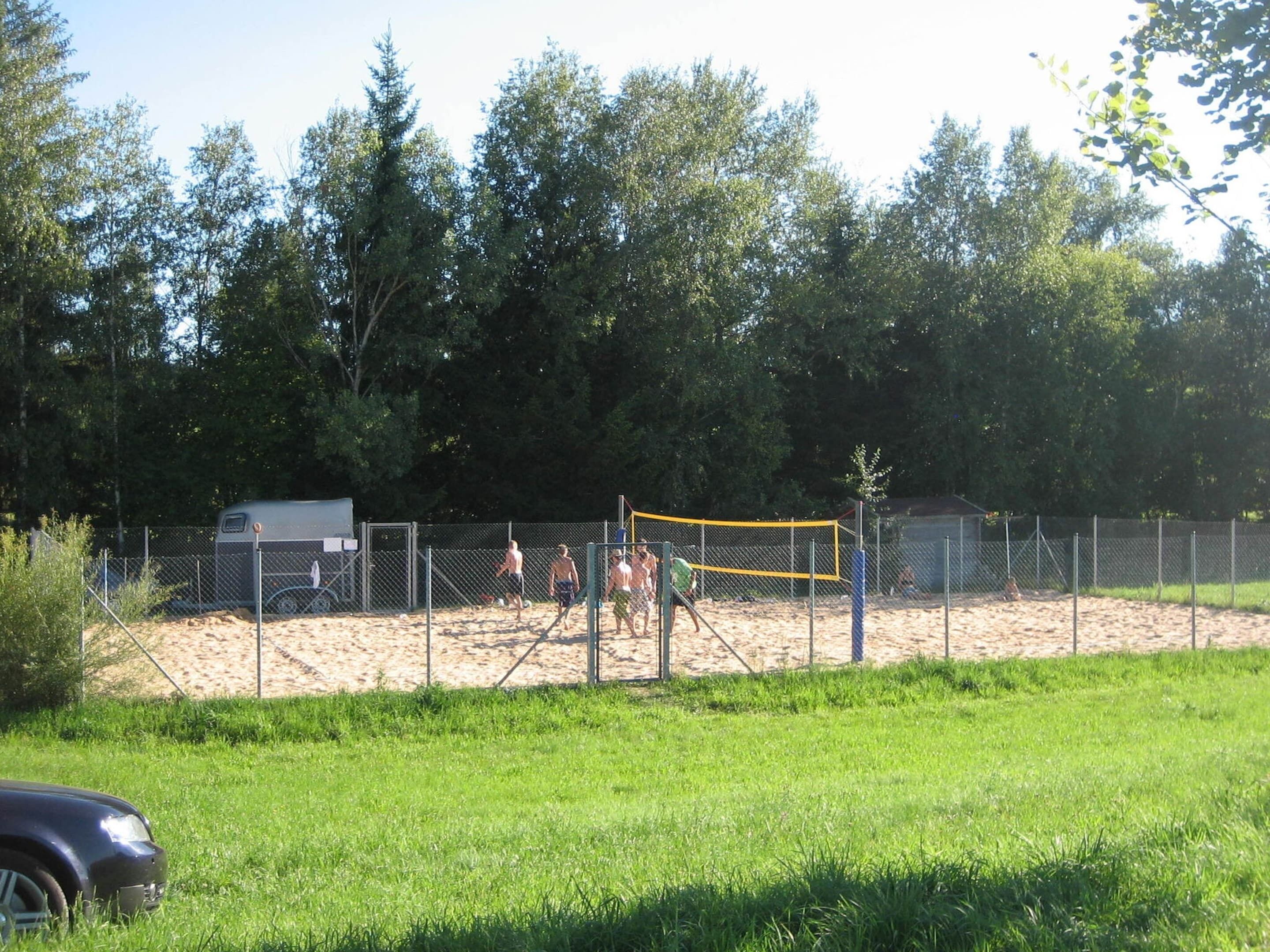 A volleyball court with a net, surrounded by a fence and trees.