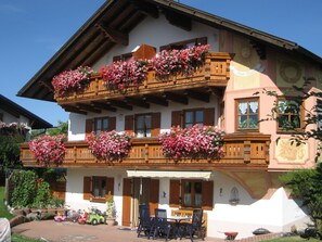 A traditional chalet with wooden balconies, a covered patio, and a garden area with toys and a lawnmower. - Apartment in the Allgau With View of the Bavarian Alps (Ingenried)