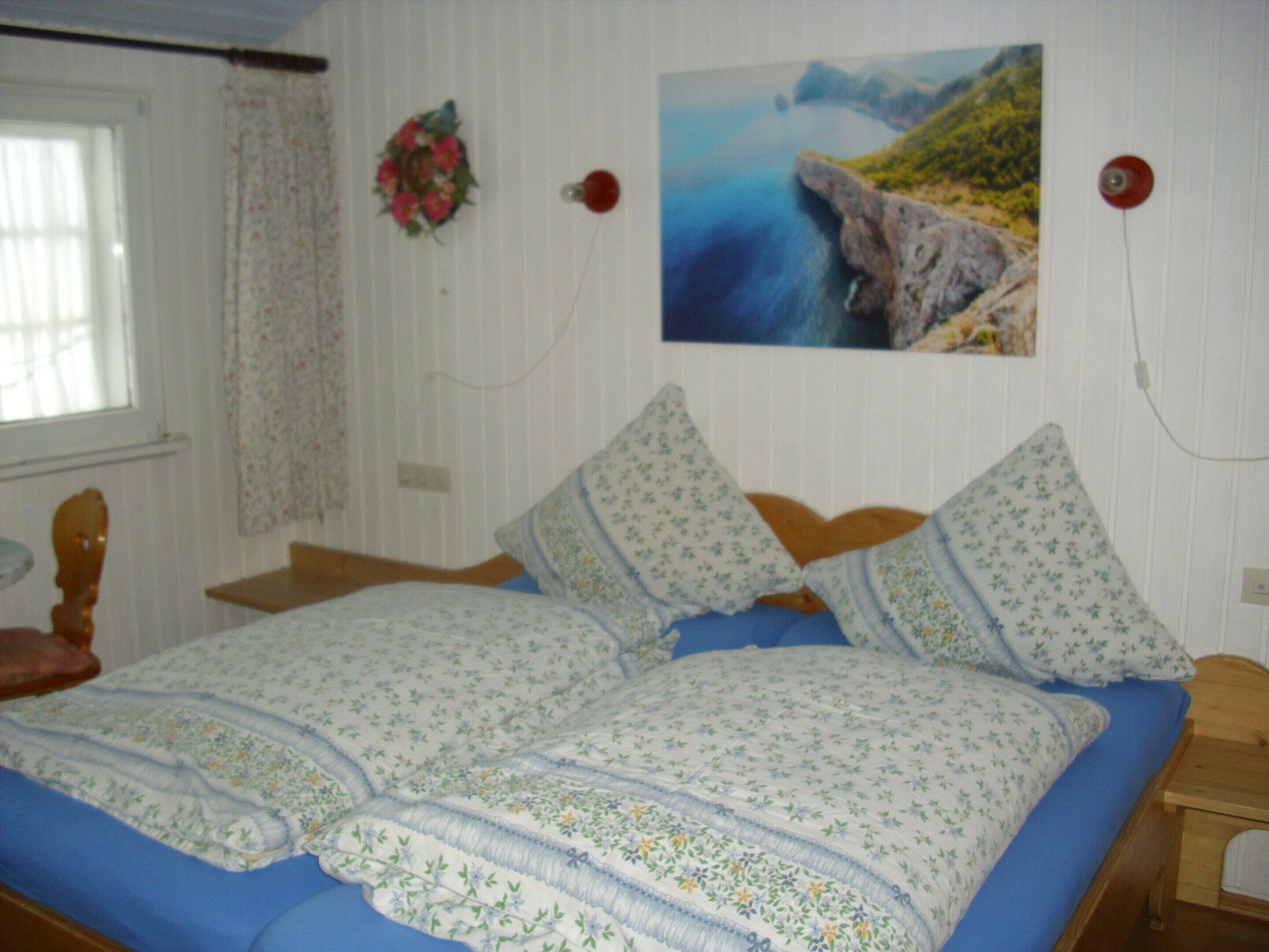 A bed with floral bedding, a wooden headboard, and a nightstand with a lamp.