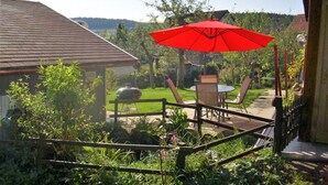 A patio area with a grill, outdoor furniture, and a red umbrella. - Beautiful Apartment in a Black Forest House With Conservatory (Bernau)