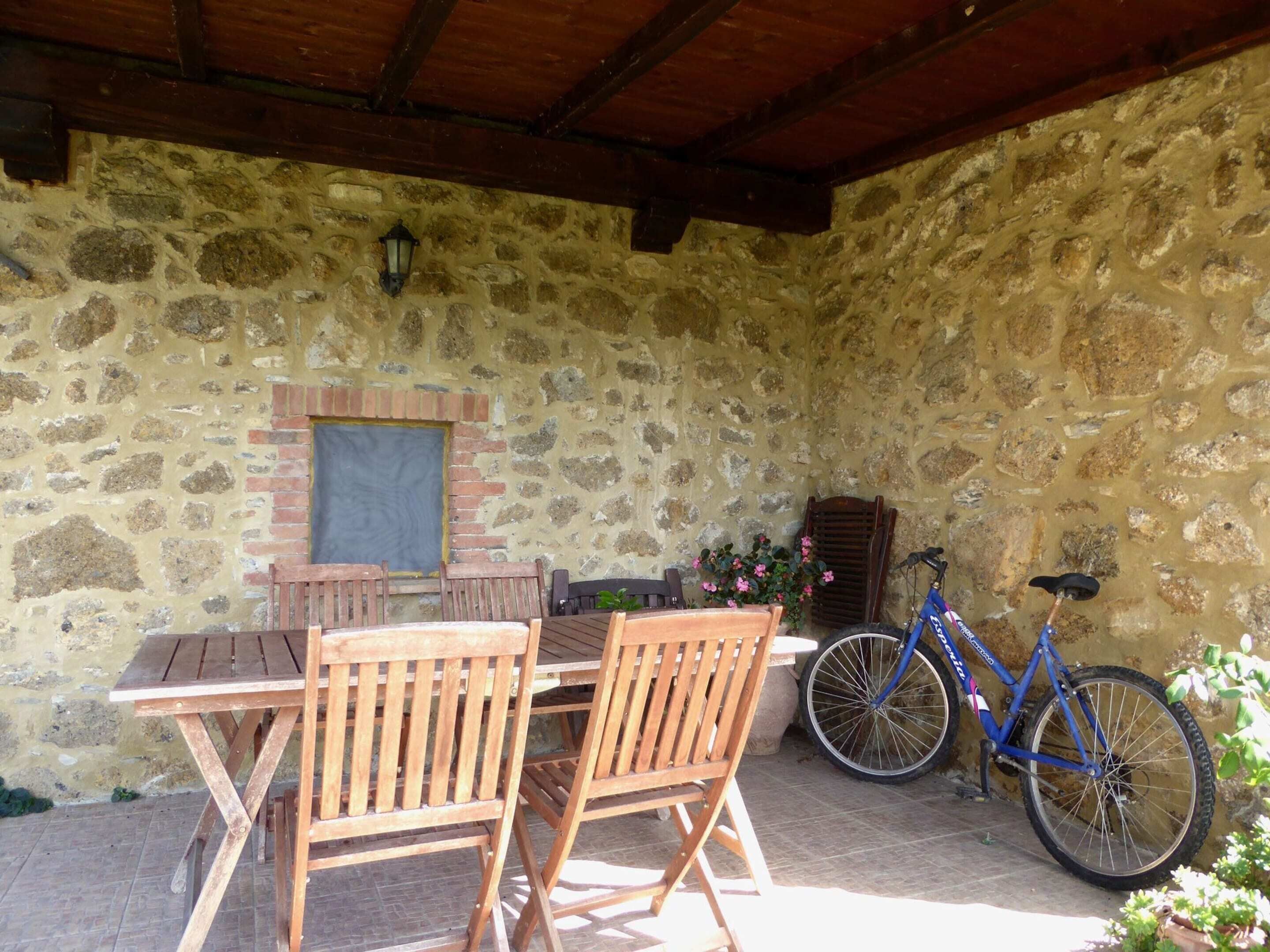 Eine Terrasse mit Steinsäulen, einem Holztisch und Stühlen, einem Fahrrad und einem Blumentopf.