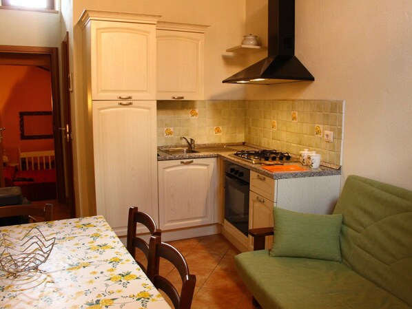 A compact kitchen with white cabinets, a gas stove, and a sink. There's a dining table with chairs and a green sofa in the corner.