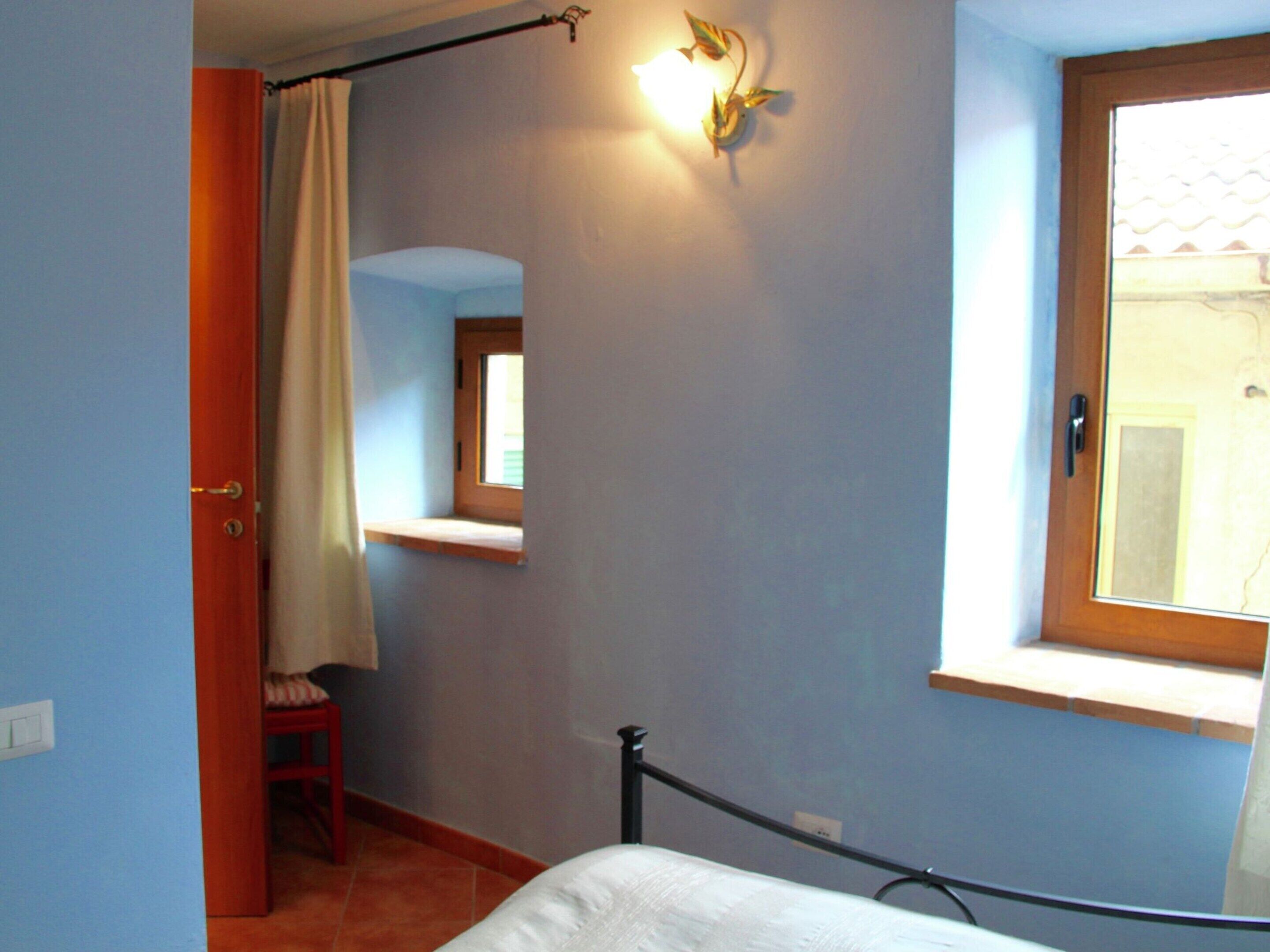 A bedroom with a bed, a window, a door, and a small window seat.