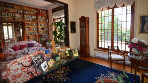 A cozy living room with a large bookshelf, a floral sofa, and a dining area with a table and chairs.