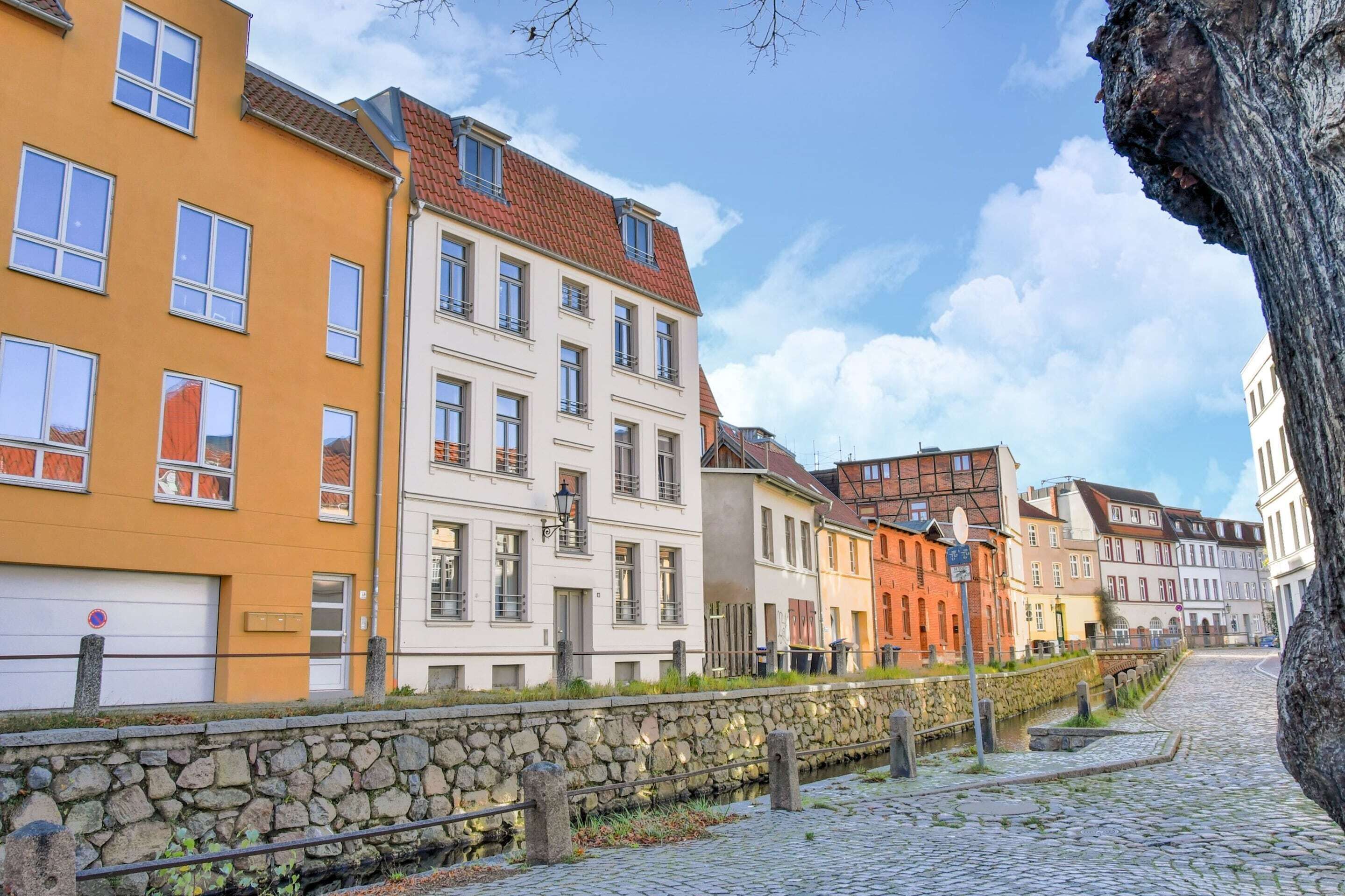 A cobblestone street lined with colorful buildings, a stone wall, and a tree.