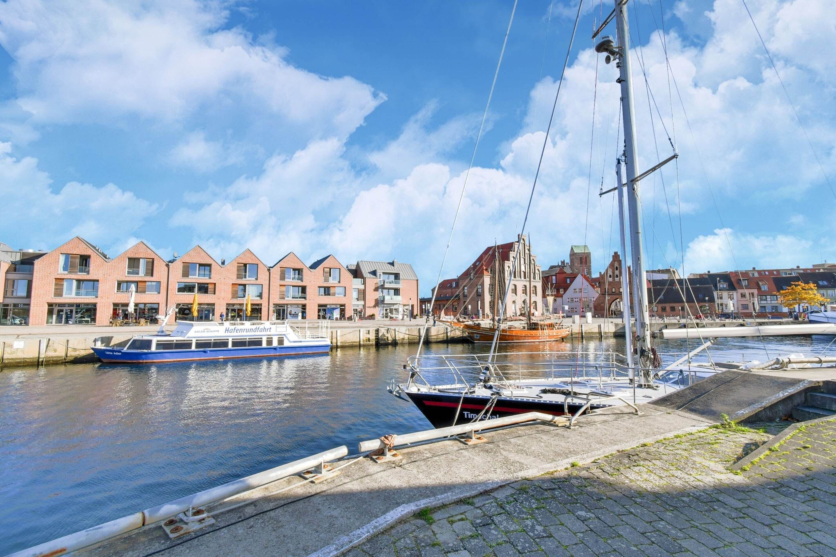 A canal with boats docked, a row of buildings with a distinctive architectural style, and a clear sky.