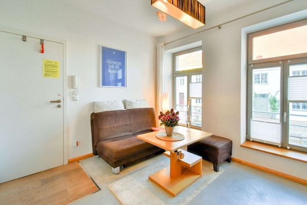 A modern living room with a brown sofa, a wooden coffee table with a vase of flowers, and a large window providing a view of the outside. - Ferienwohnung in Wismar im Stadtzentrum (Wismar)