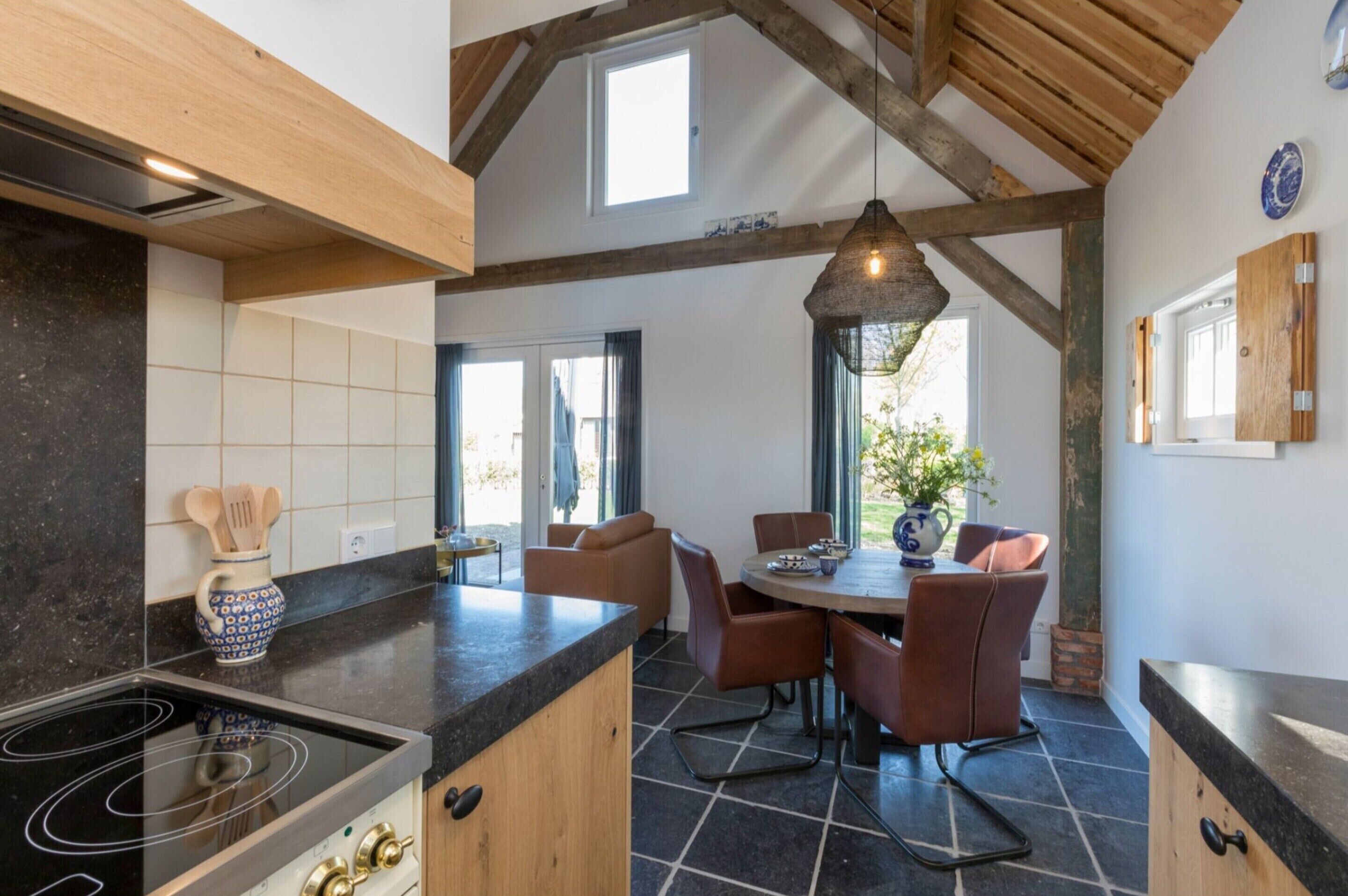A modern kitchen with a large island, wooden beams, and a dining area with brown chairs.