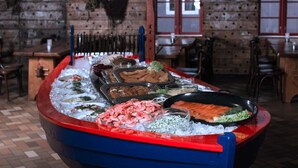A seafood buffet with various dishes displayed on ice, set in a rustic restaurant with brick walls and wooden furniture. - 6 Person Holiday Home in Allinge (Gudhjem)