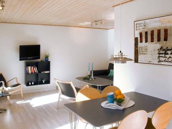 Un salon moderne avec un téléviseur à écran plat, une bibliothèque, une table à manger avec des chaises et un grand tableau accroché au mur.