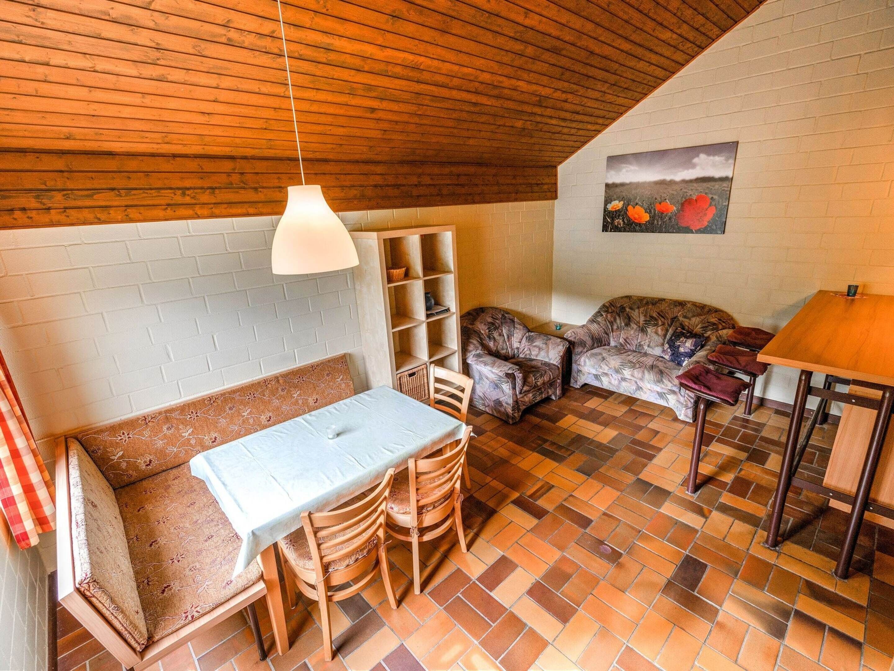 A cozy room with a wooden ceiling, a white brick wall, a sofa, a table, and a chair.