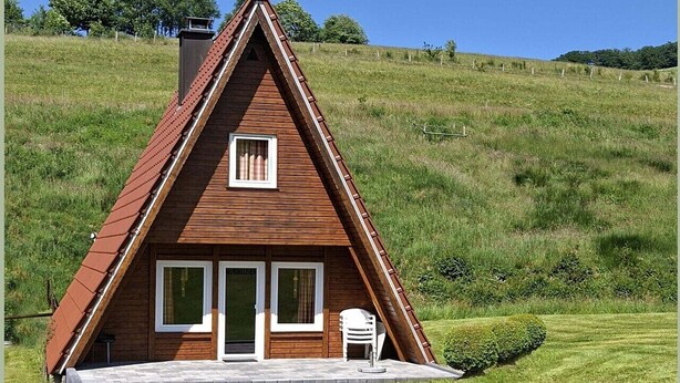 Une maison en bois avec un toit en pente, une entrée pavée et un petit patio avec une chaise.