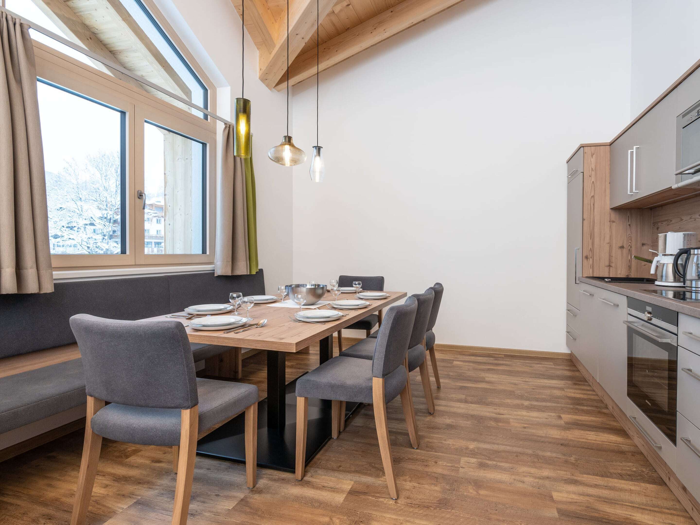 A modern kitchen with wooden cabinets, a dining table set for four, and a large window with curtains.