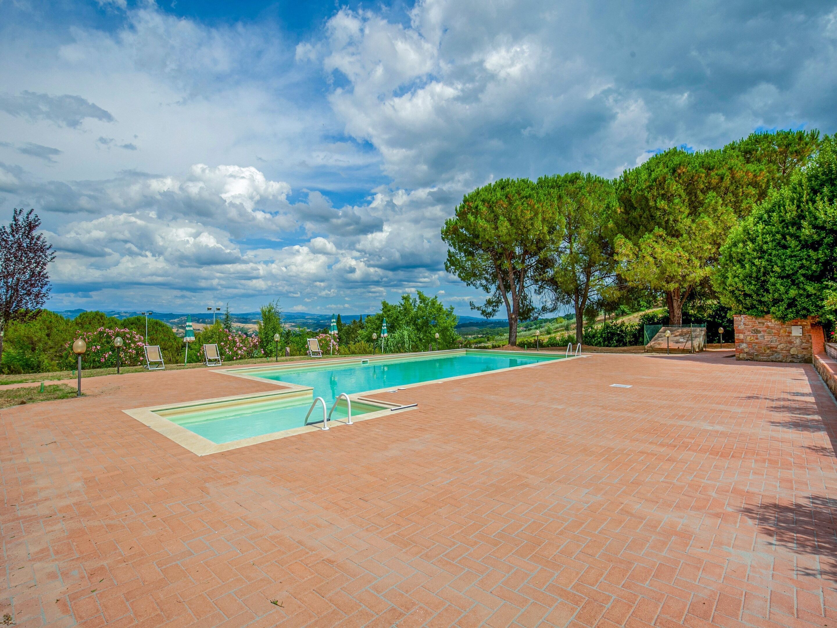 Una piscina rectangular con solárium de ladrillo, rodeada de árboles y con vistas a colinas distantes.