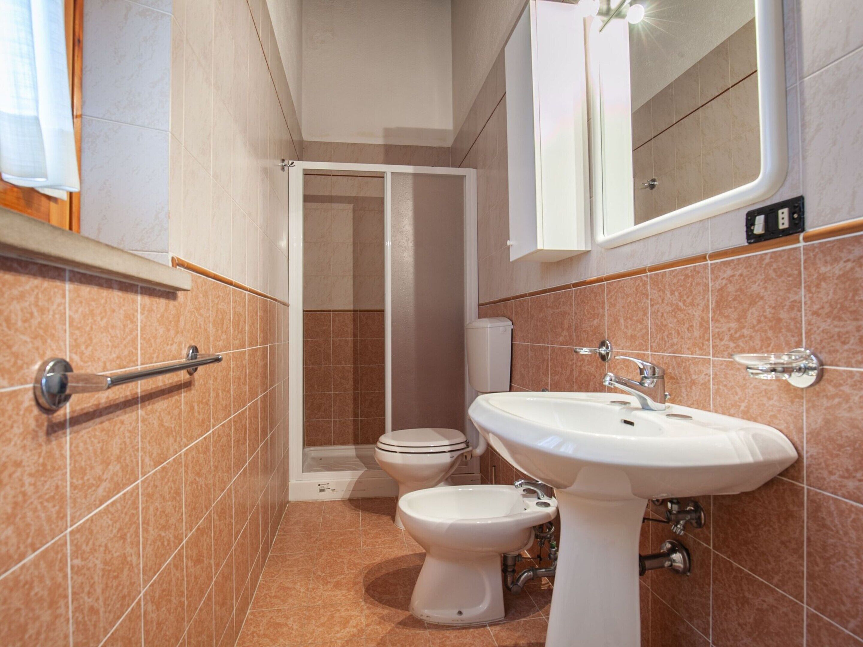 Ein Badezimmer mit Toilette, Bidet und Waschbecken, mit gefliesten Wänden und einem Spiegel über dem Waschbecken.