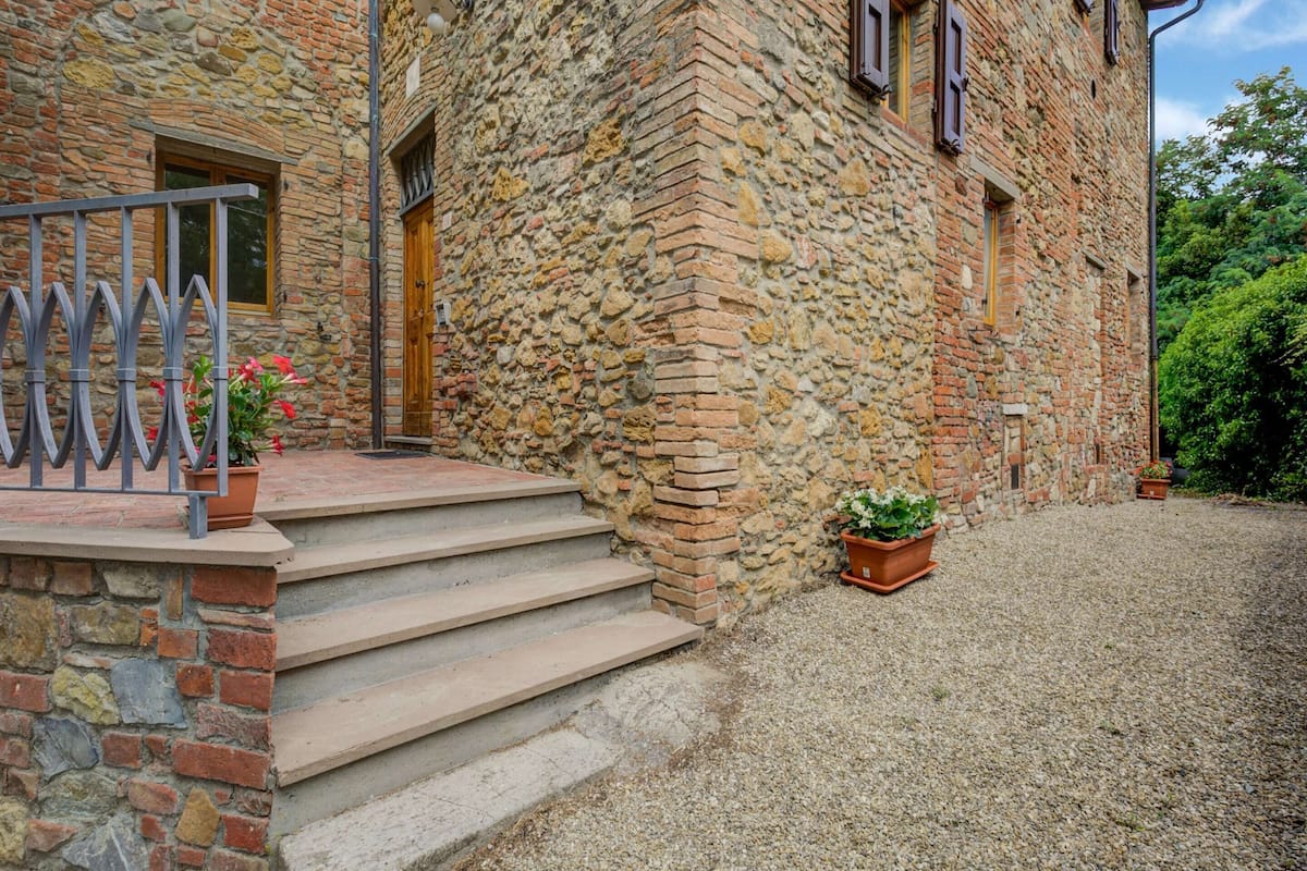 A stone building with a wooden door, steps leading to a gravel driveway, and a metal railing.