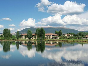 A lakeside view with houses reflecting on the water, surrounded by trees and mountains in the background. - Pleasant Apartment in Santa Maria Degli Angeli With Pool (Assisi)