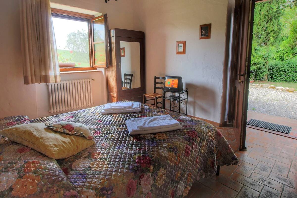 A bedroom with a bed, a chair, a television, and a view of the outdoors.