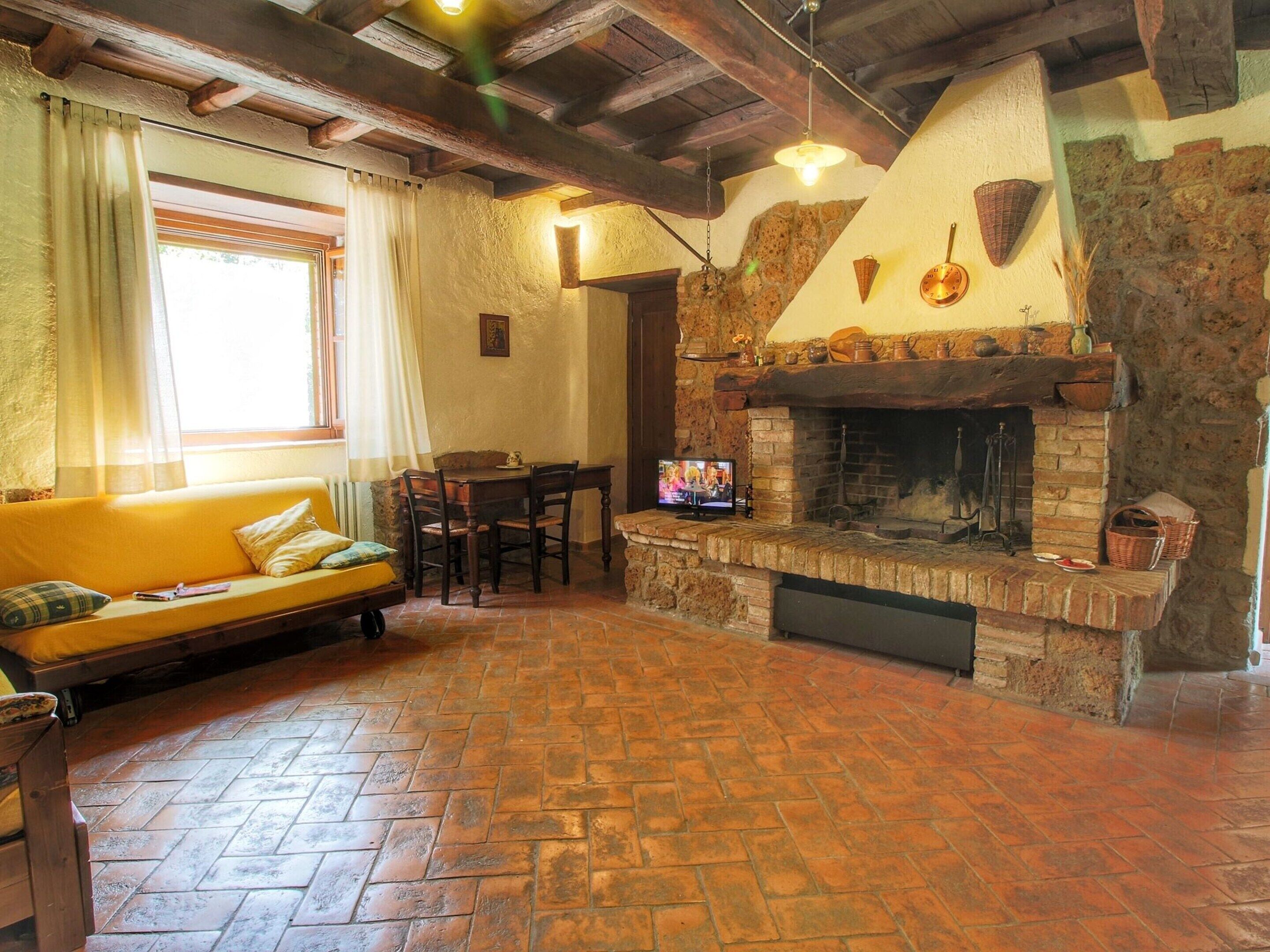 A cozy living room with a stone fireplace, wooden beams, a sofa, and a television.